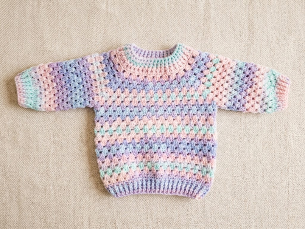 Suéter infantil em crochê artesanal com mangas longas e trama em tons pastel degradê.